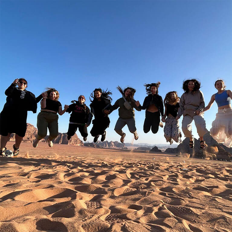 People are smiling and jumping in the desert.