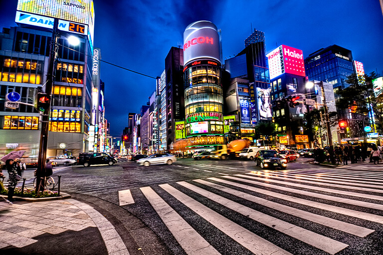 An intersection at night in Tokyo filled with cars and people on the sidewalks.